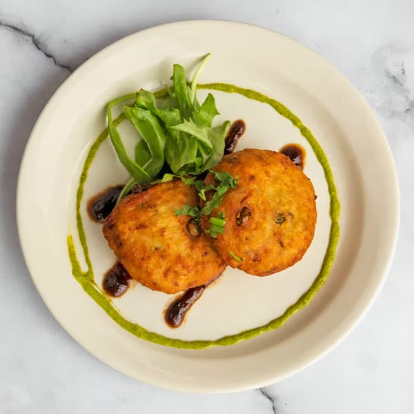 Two golden-brown Indian cutlets with green and brown sauces, garnished with fresh greens.