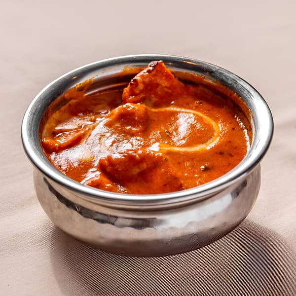 A silver bowl filled with vibrant orange Indian butter chicken, garnished with a swirl of cream.
