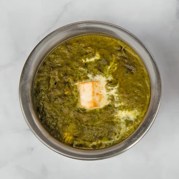 Overhead view of Palak Paneer, a vibrant green Indian spinach and cheese curry, in a metal bowl.