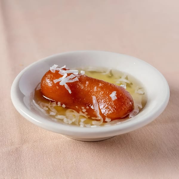 A single gulab jamun, an Indian dessert, in a white bowl with syrup and coconut flakes.