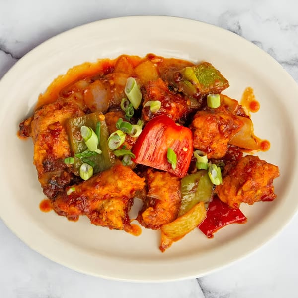Indian chili chicken with bell peppers and green onions on a white plate.