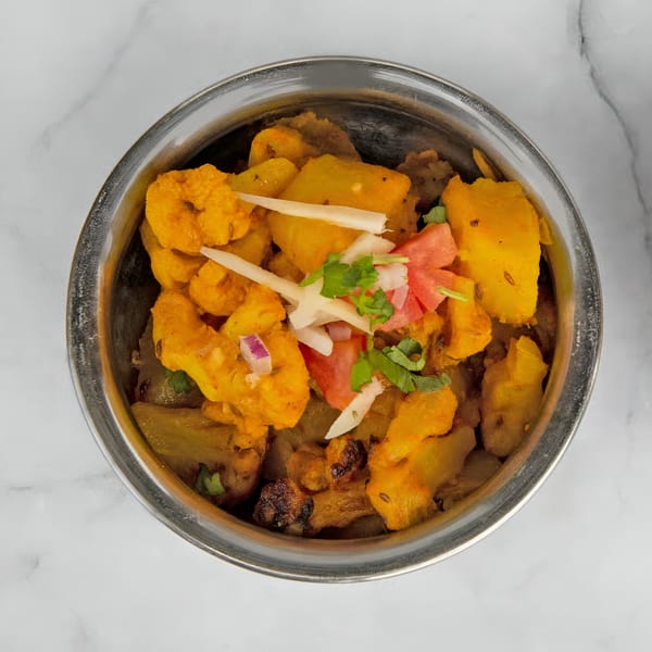 Aloo Gobi, an Indian dish with spiced potatoes and cauliflower, garnished with fresh herbs and onions.